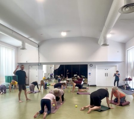 Group exploring hands-and-knees movement with tennis balls as Ian teaches